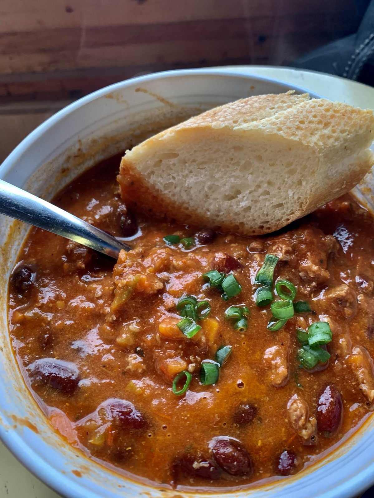 A bowl of chili topped with green onion, served with fresh bread