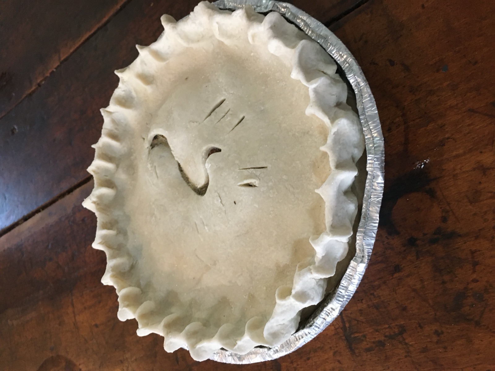 A hand-crimped pie on a wooden table, ready for the oven